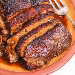 Juicy braised pork roast with caramelized onions on a rustic terracotta dish.