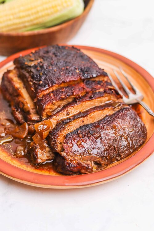 Braised beef pot roast with onions and gravy on a rustic clay plate.