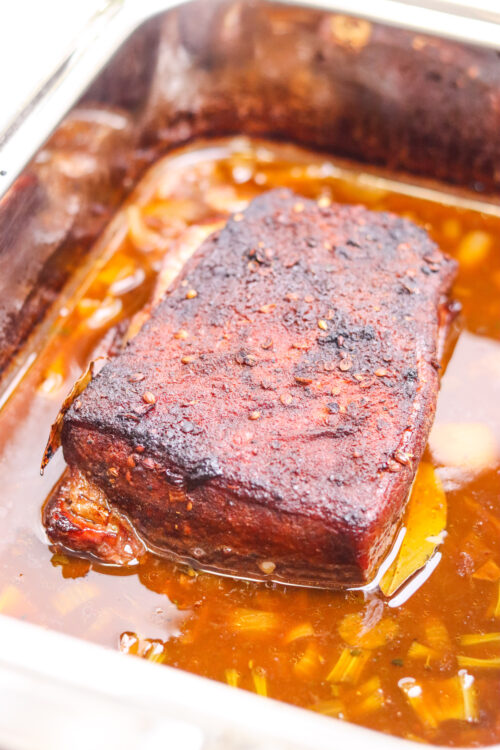 Juicy, tender beef roast cooking in a flavorful broth in a roasting pan.