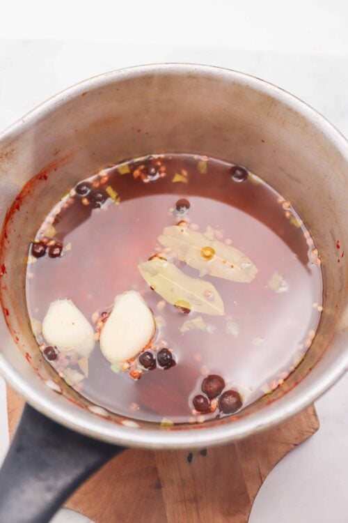 Brine with garlic, peppercorns, and bay leaves in a stainless steel pot.