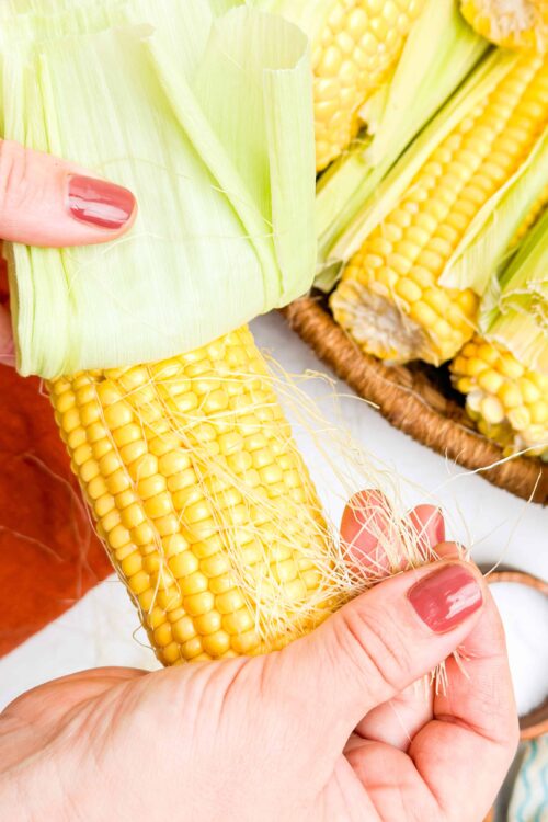 Fresh yellow corn on the cob with husk partially removed, highlighting its vibrant kernels and silky threads.