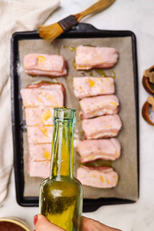 Buttered pork chops on baking sheet with olive oil, ready for baking.