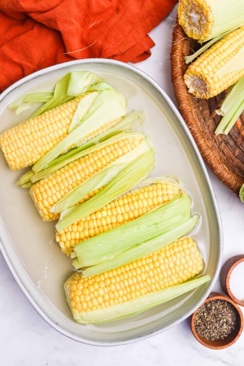 Fresh sweet corn on the cob in a white baking dish, ready for boiling or grilling.