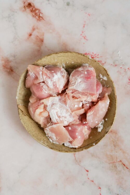 Raw chicken pieces in a rustic wooden bowl on a marble surface.