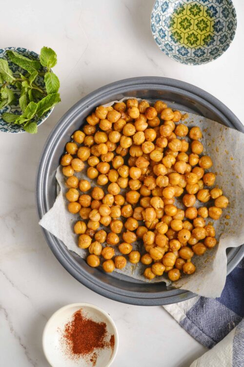 Crunchy roasted chickpeas on parchment paper in a baking dish with fresh mint and spices.