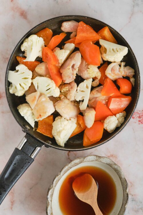 Cooked chicken, cauliflower, and carrots in a skillet for healthy meal prep.