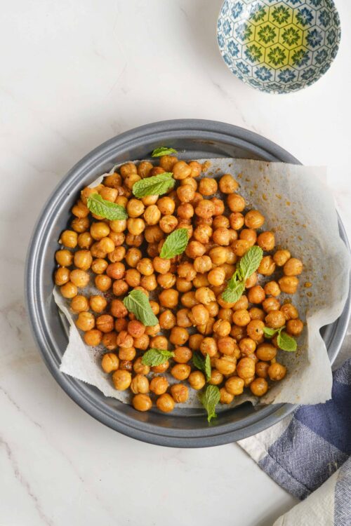 Roasted chickpeas garnished with fresh mint leaves on a baking sheet.