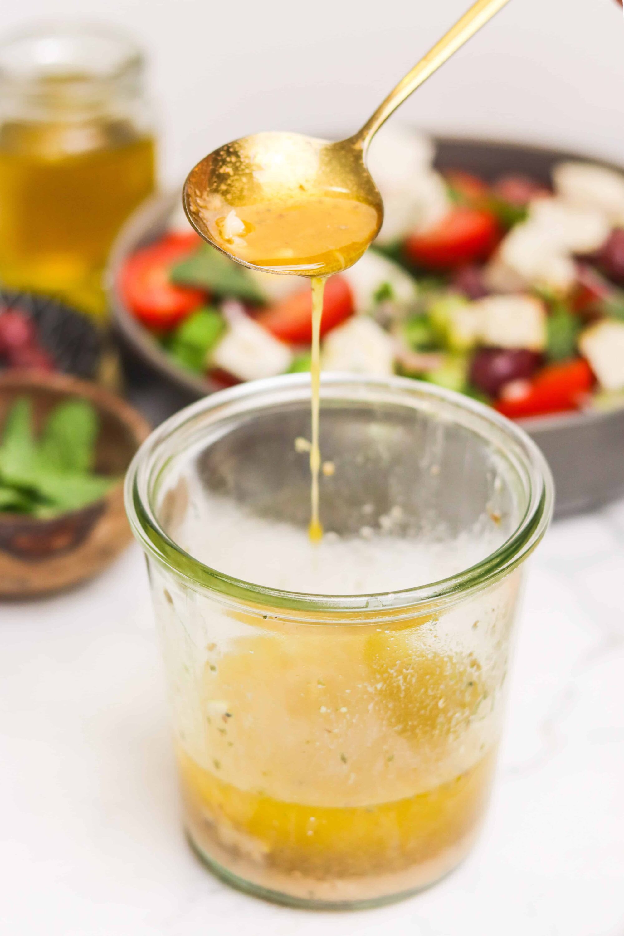 Rich honey being drizzled from a spoon into a glass jar, with fresh salad ingredients in the background.