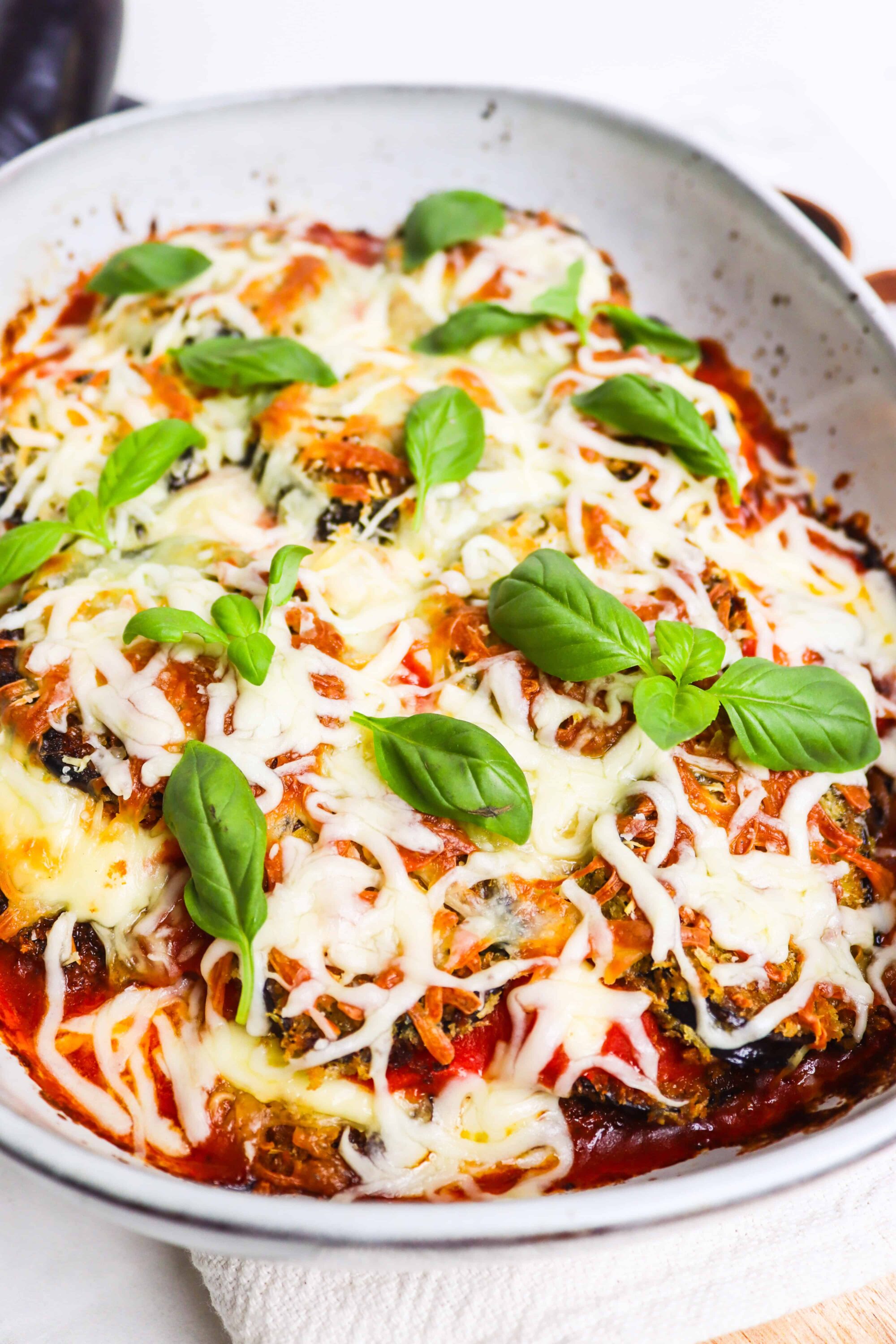 Baked ziti with melted cheese and fresh basil garnishing, in a white baking dish.