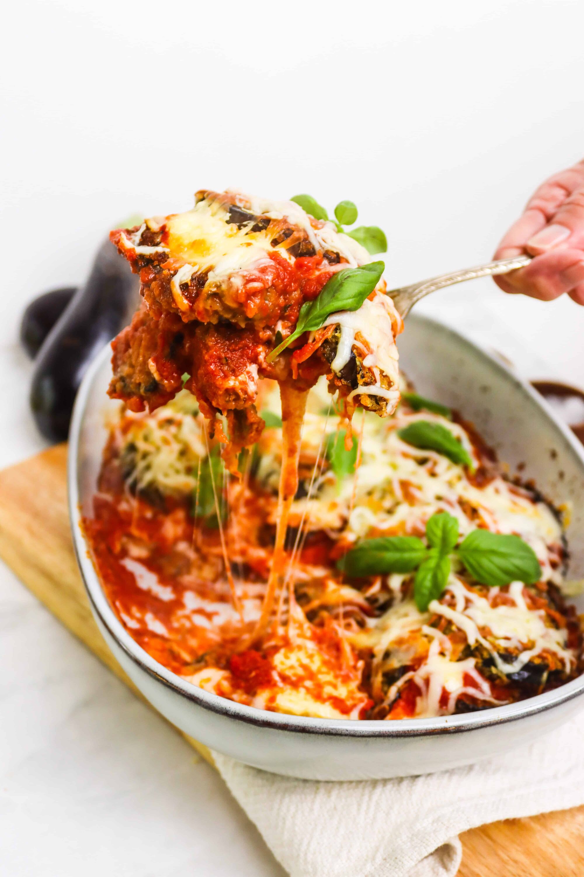 Hearty baked eggplant parmesan with melted cheese and fresh basil, served in a white baking dish.