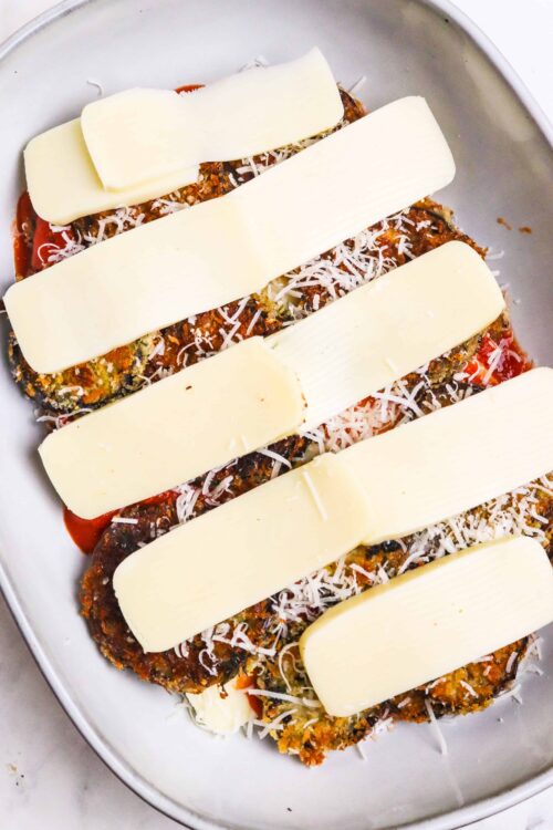 Golden baked eggplant parmesan with melted cheese and fresh grated parmesan on top, ready to bake.