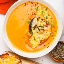 Creamy tomato basil soup served with cheese toast on a white plate, perfect for comforting meals.