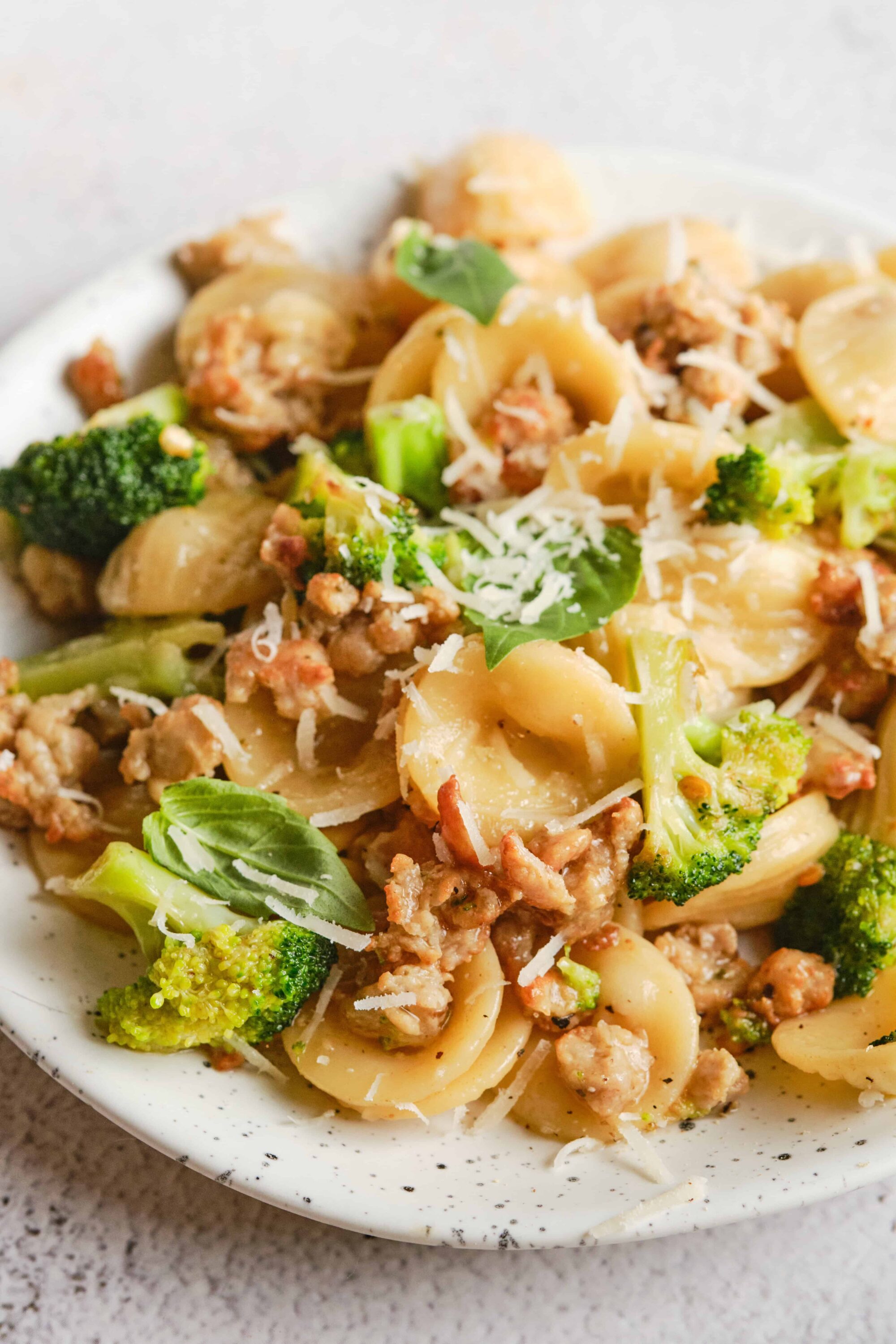 Creamy pasta with broccoli, sausage, and grated cheese in a white bowl.