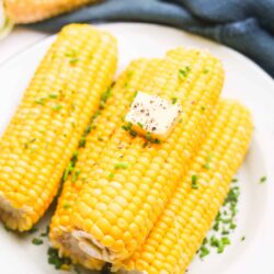 Golden corn on the cob with butter and chives on a white plate, fresh and ready to serve.