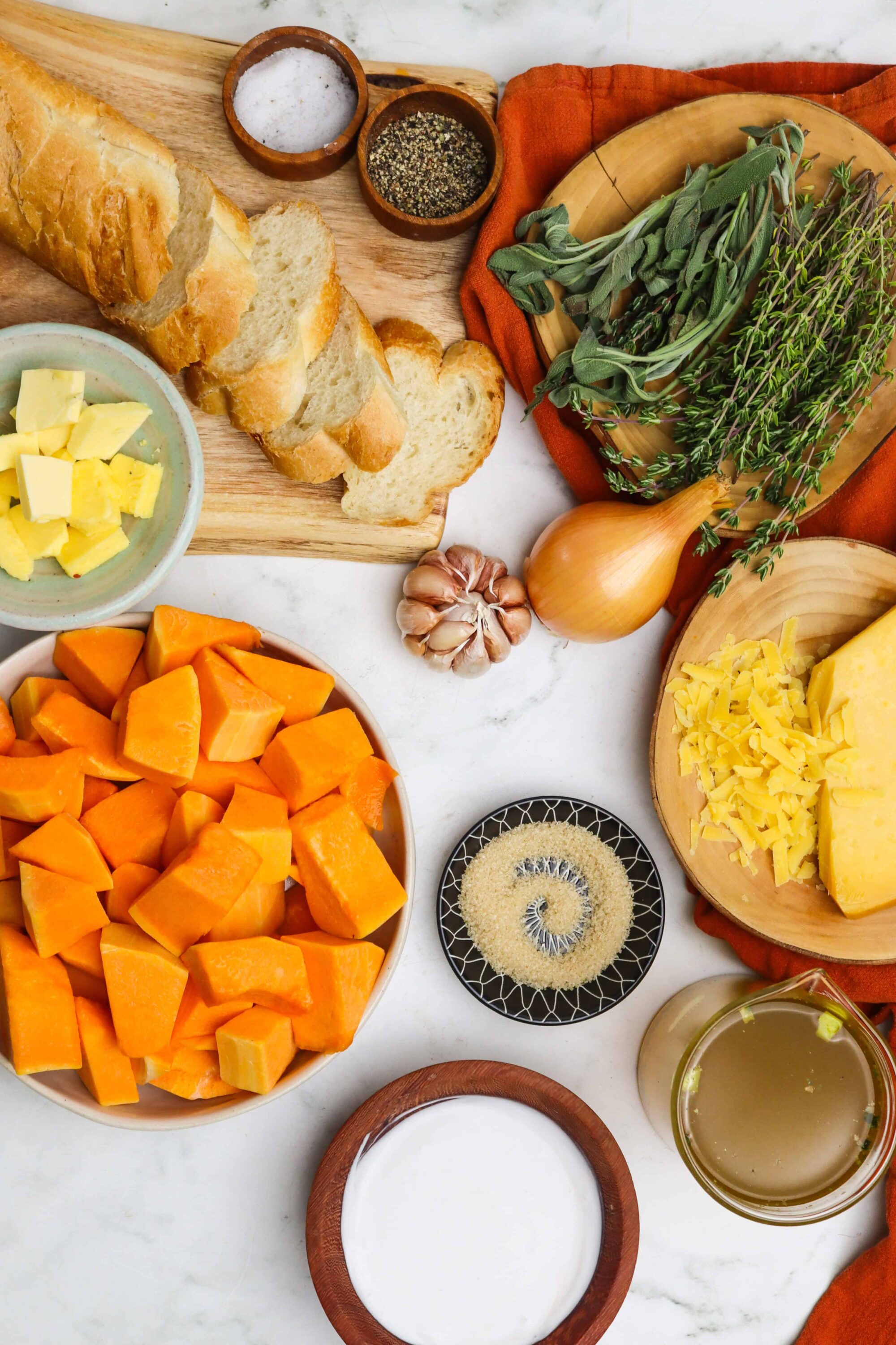 Fresh butternut squash, bread, cheese, herbs, garlic, and spices for autumn comforting soup or recipe ingredients.