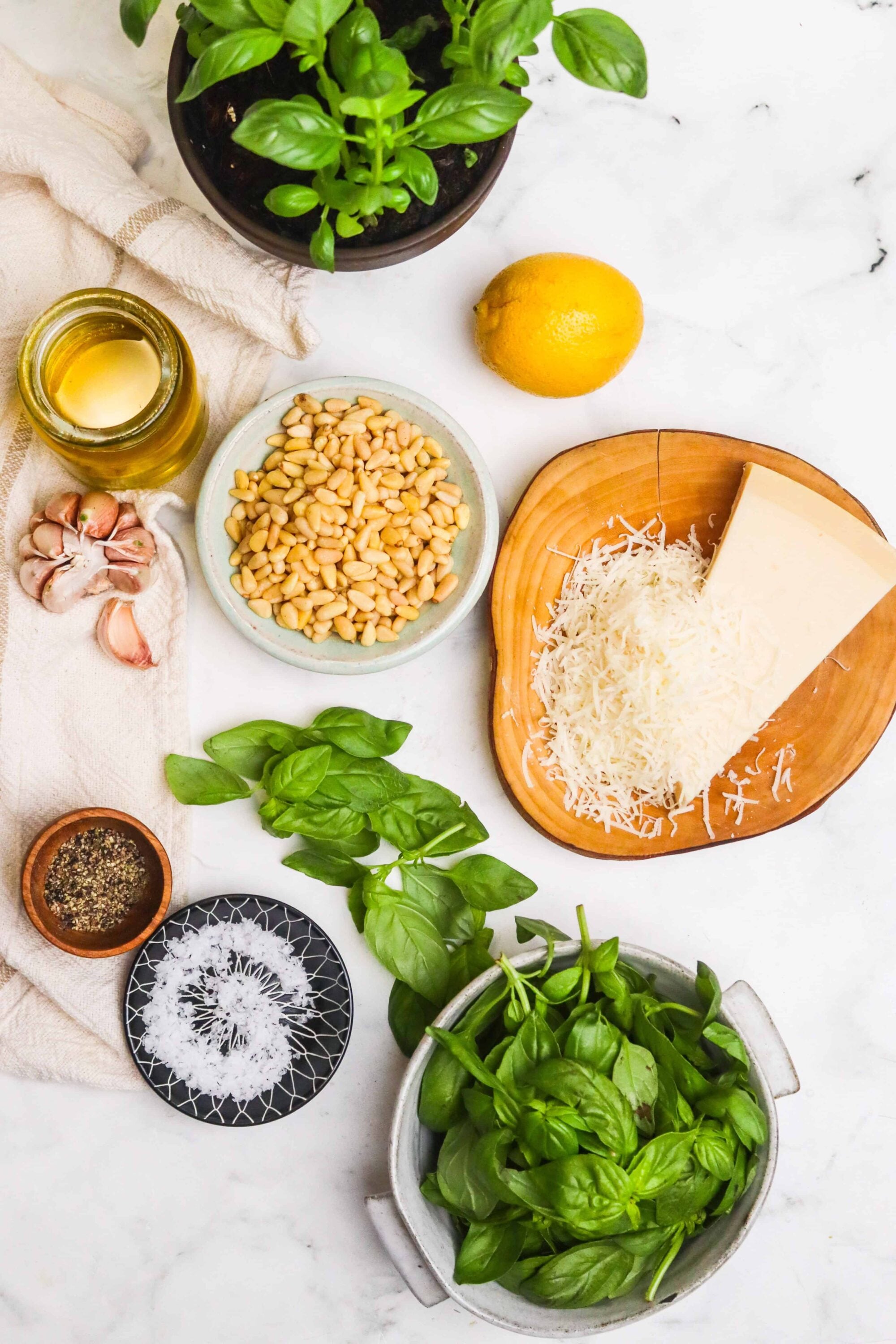 Fresh basil, garlic, pine nuts, grated cheese, lemon, olive oil, and seasonings for homemade pesto on white marble.