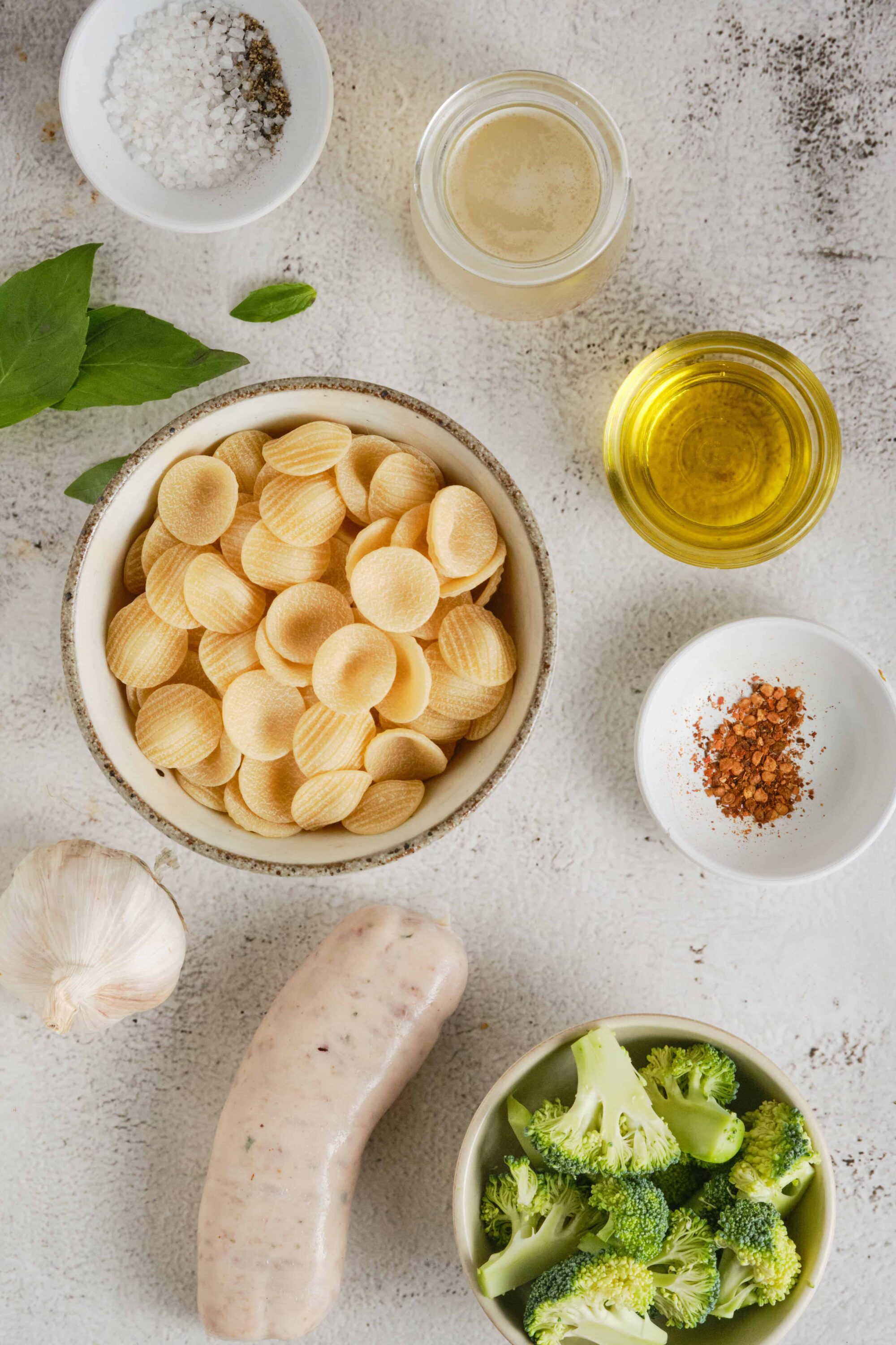 Softened white beans for creamy soup recipe, with garlic, herbs, broth, and vegetables on textured background.