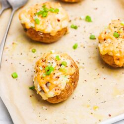 Baked cheesy stuffed potatoes with cheese and green onions on baking sheet, delicious savory appetizer or side dish.