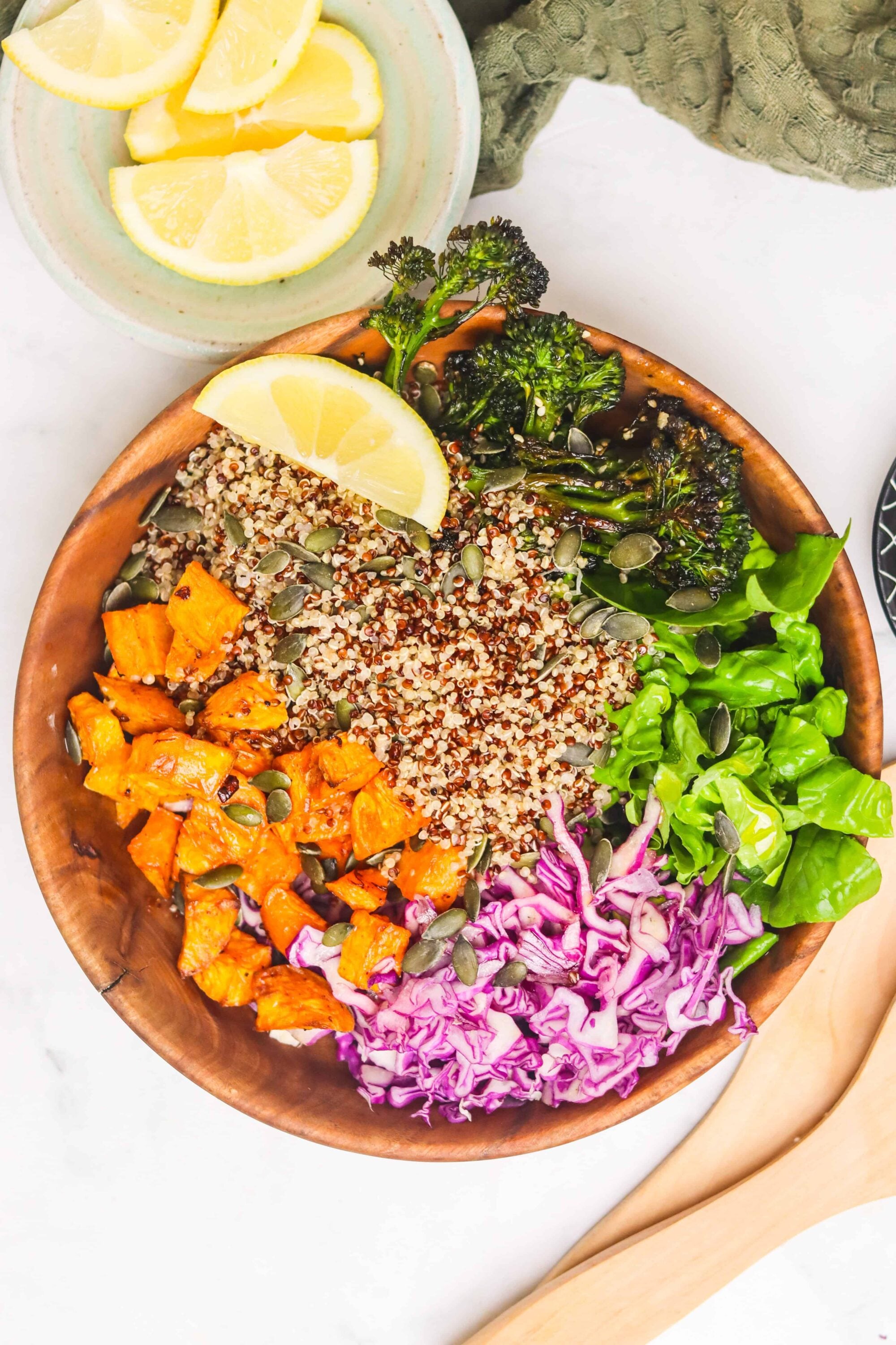 Fresh colorful quinoa salad with roasted vegetables, greens, and lemon slices, served in a wooden bowl.