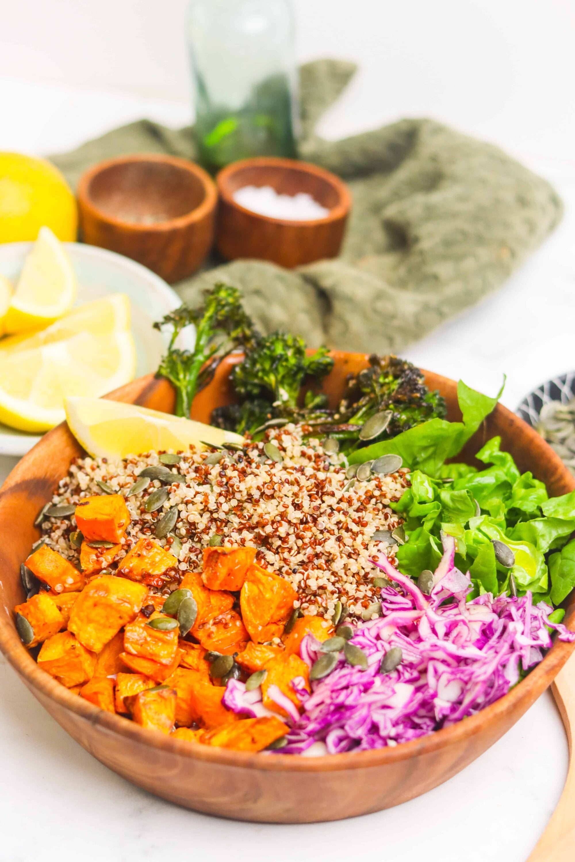 Fresh vegan quinoa salad with roasted sweet potatoes, greens, and colorful vegetables in a wooden bowl.