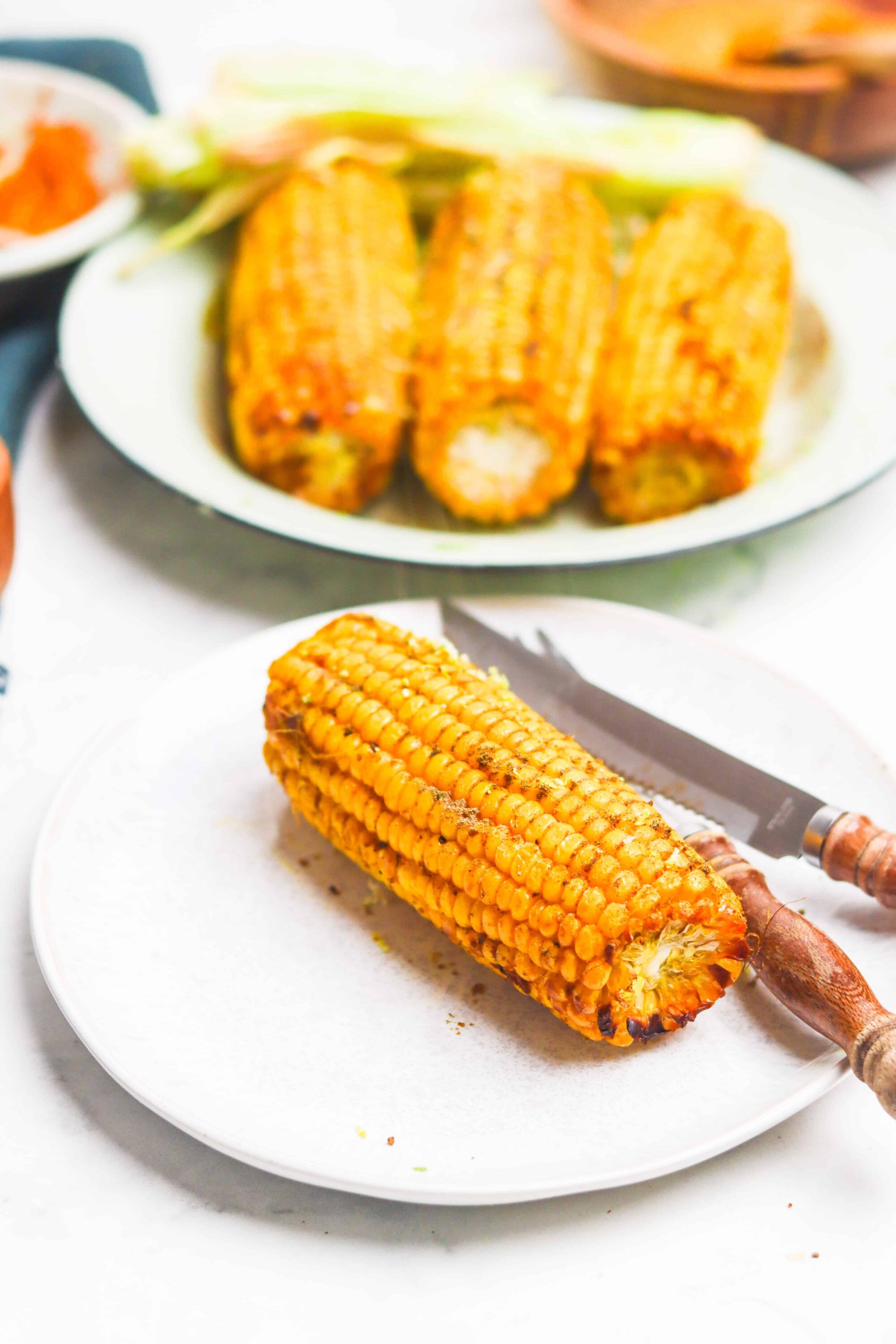 Grilled corn on white plate with a knife, fresh roasted corn, summer bbq side dish, delicious charred corn, flavorful grilled corn.
