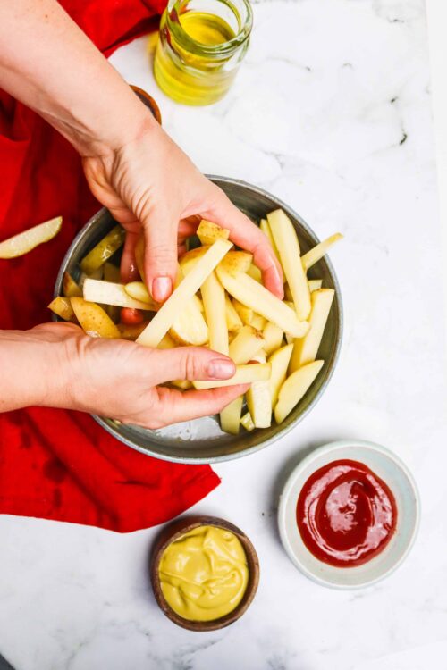 Fresh cut potato fries being prepared for baking or frying on a white marble countertop.