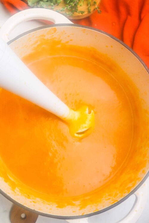 Creamy butternut squash soup with smooth texture in a white pot, ready to serve.