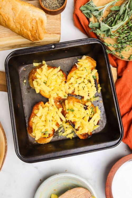 Baked eggplant slices topped with shredded cheese and herbs in a baking dish.