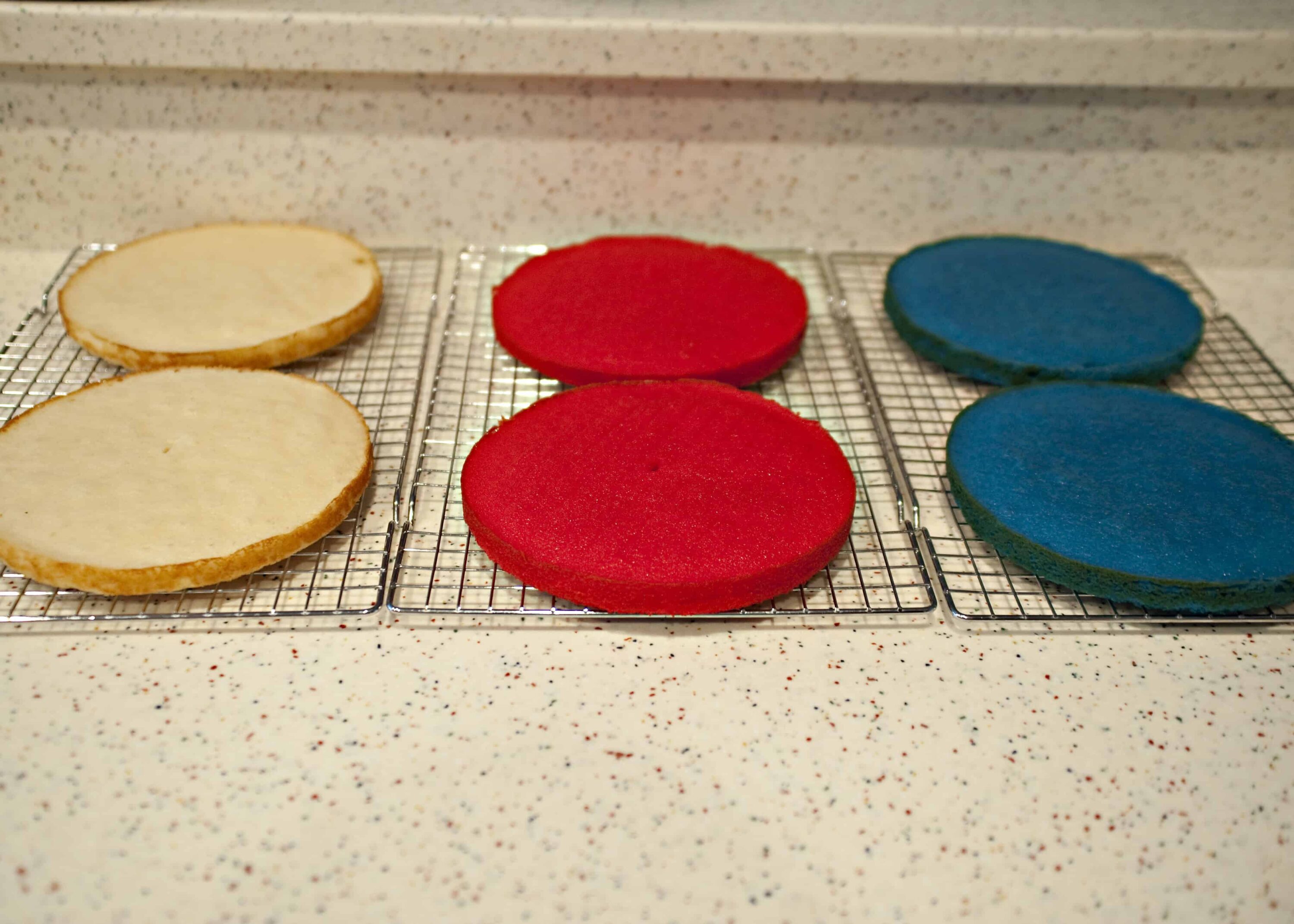 Foam cookie cutters in red, blue, and white on cooling racks with a speckled countertop background|red, blue, and white foam cookie cutters cooling on racks|Colorful foam cookie cutters in red, blue, and white cooling on wire racks, ready for baking or crafting projects|A set of foam cookie cutters in red, blue, and white arranged on wire cooling racks on a speckled countertop, suitable for baking or kids' crafts|relevance.