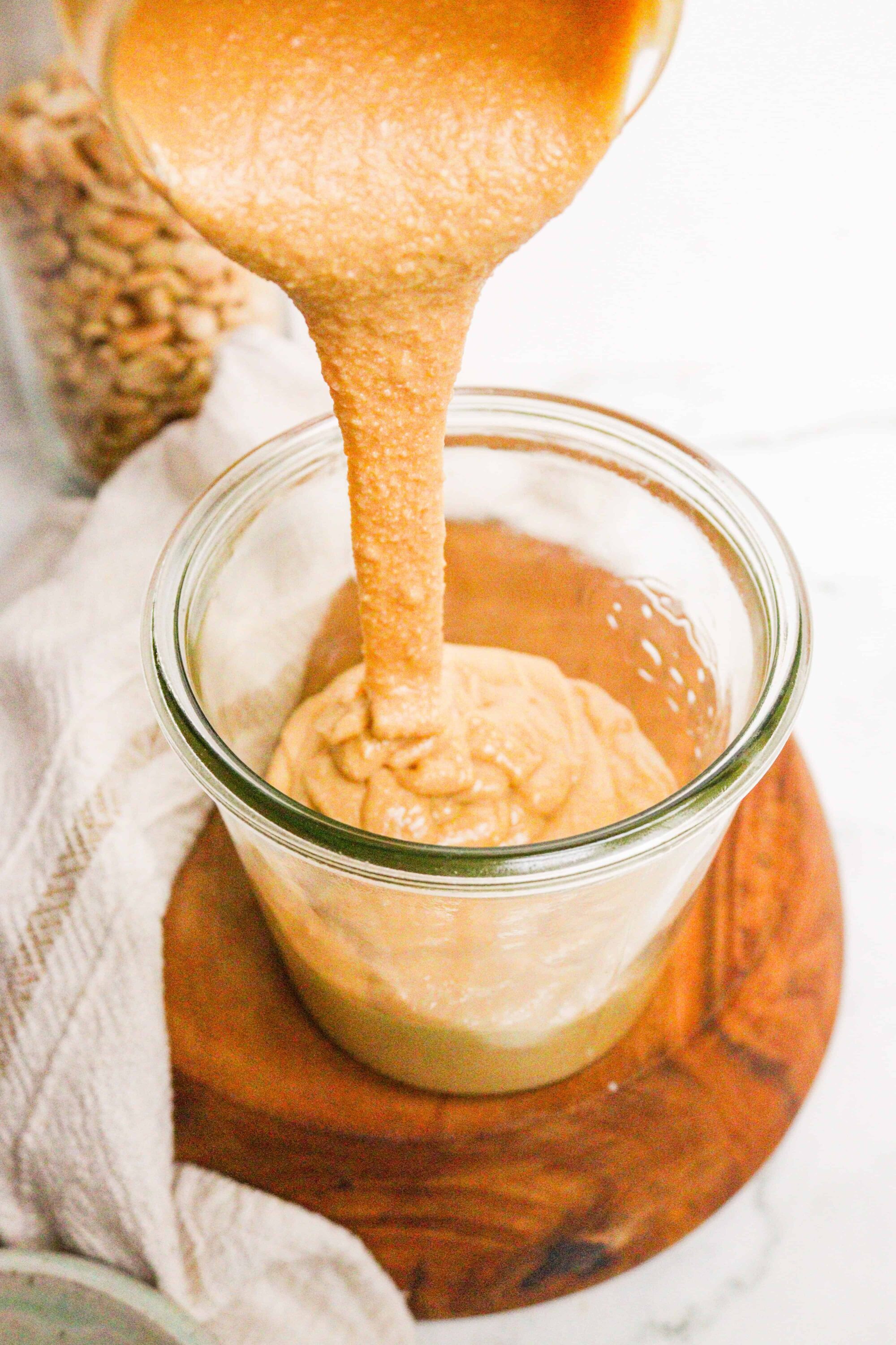 Crushed graham crackers being poured into a jar of homemade peanut butter caramel spread.