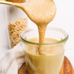 Creamy peanut butter caramel sauce drizzling from a spoon into a glass jar.