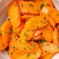 Steamed & sliced carrots garnished with chopped green herbs on a white dish.