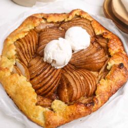 Sweet pear galette with sliced pears and vanilla ice cream on a rustic white surface. Perfect dessert from Baked Bree.
