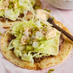 Fresh ground beef and cheese tacos topped with shredded lettuce, chopped onions, and chopped pickles on soft tortillas.