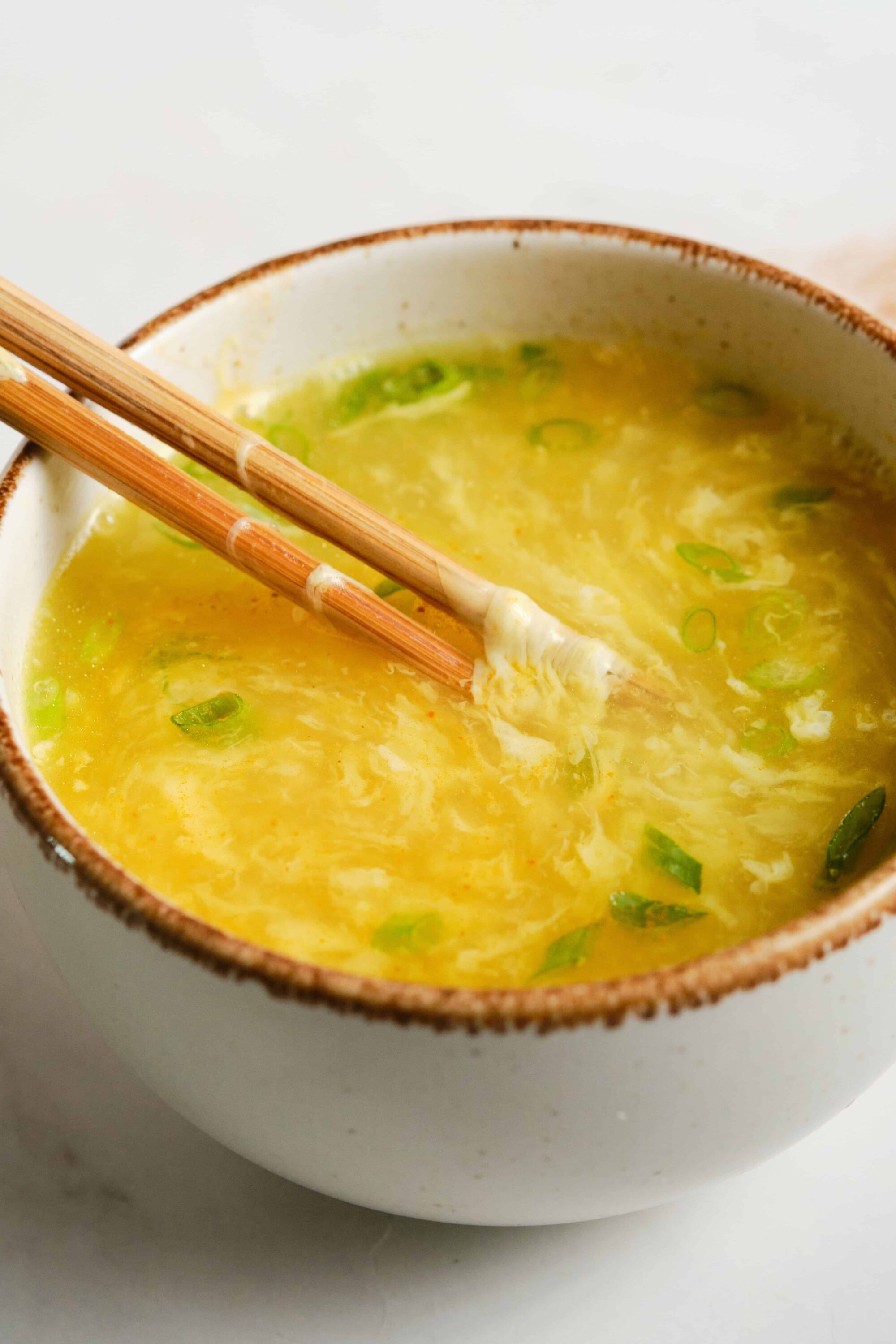 Steamed egg drop soup with chopped green onions in a rustic bowl.