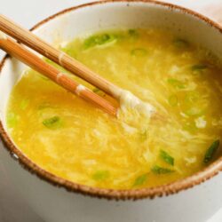 Steamed egg drop soup with chopped green onions in a rustic bowl.