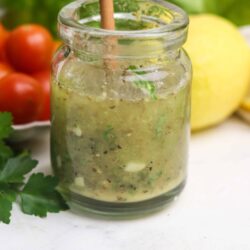 Fresh homemade green salsa in a glass jar with fresh produce in the background, perfect for taco night or as a dip.