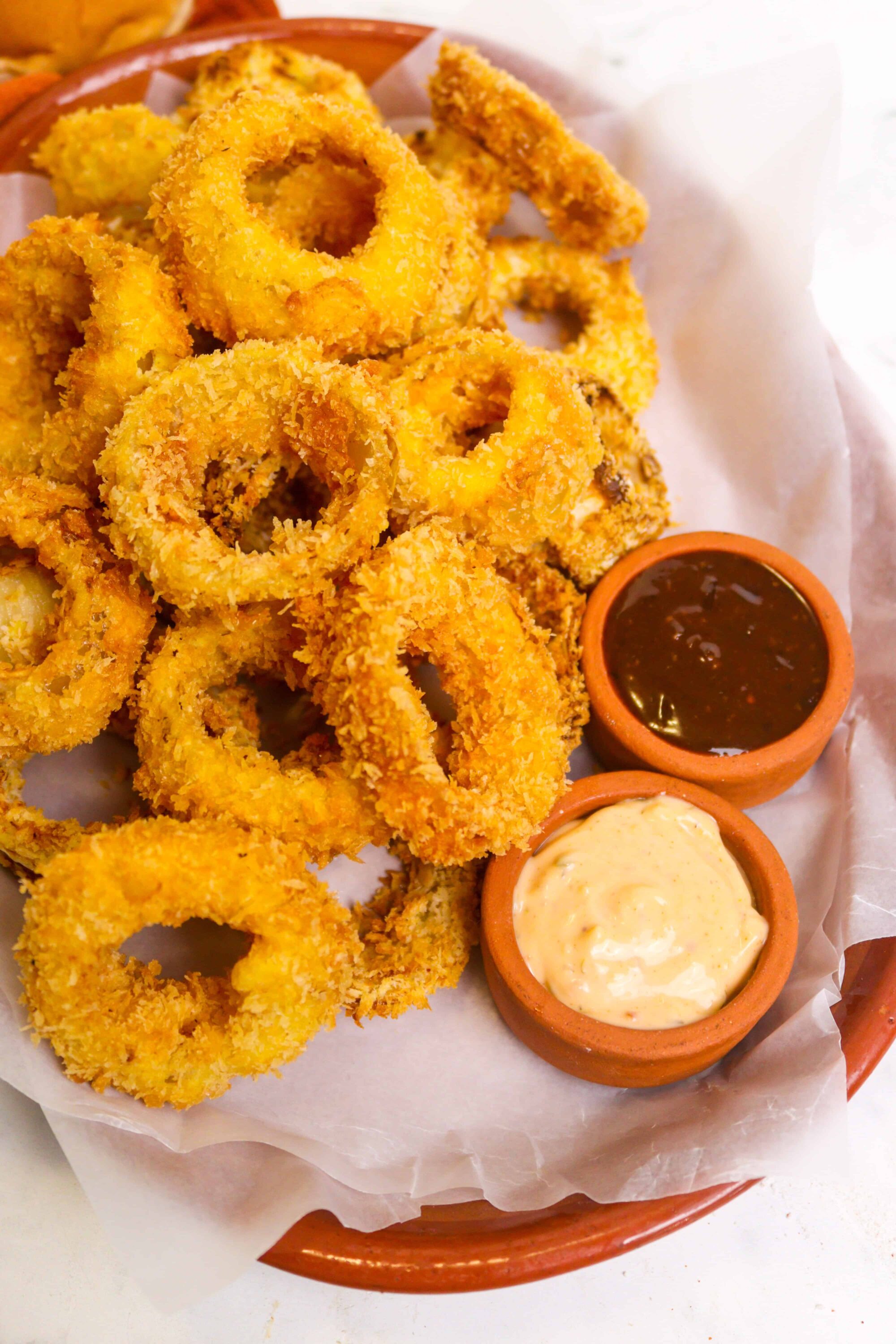 Golden crispy onion rings with dipping sauces in a basket.