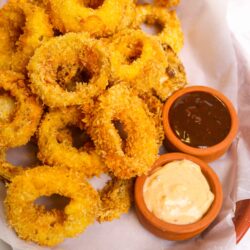 Golden crispy onion rings with dipping sauces in a basket.