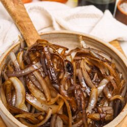 Caramelized roasted onion dish in a rustic bowl with fresh onions and cooking ingredients in background.