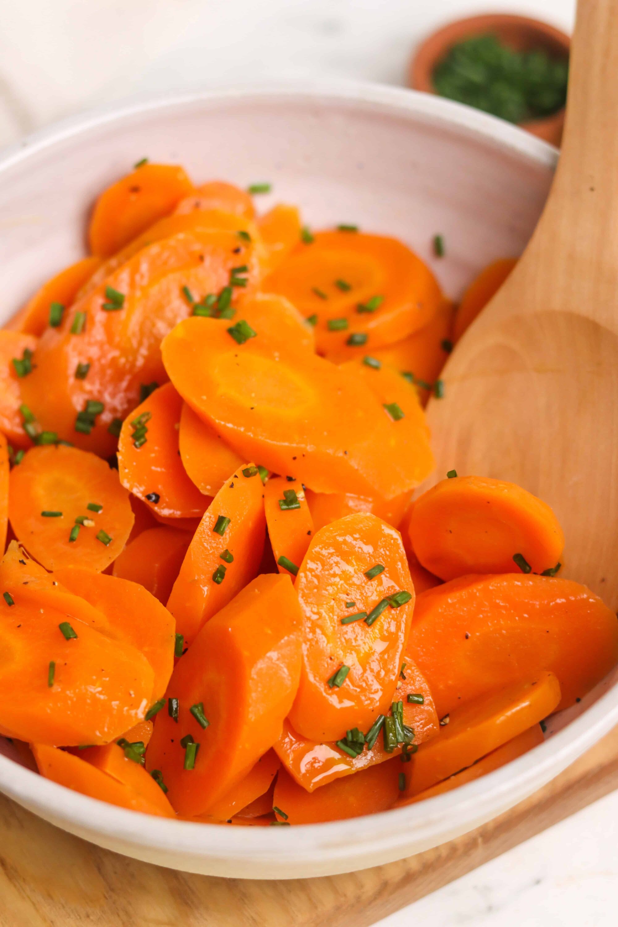 Sweet glazed carrots with chopped chives in a white serving bowl.