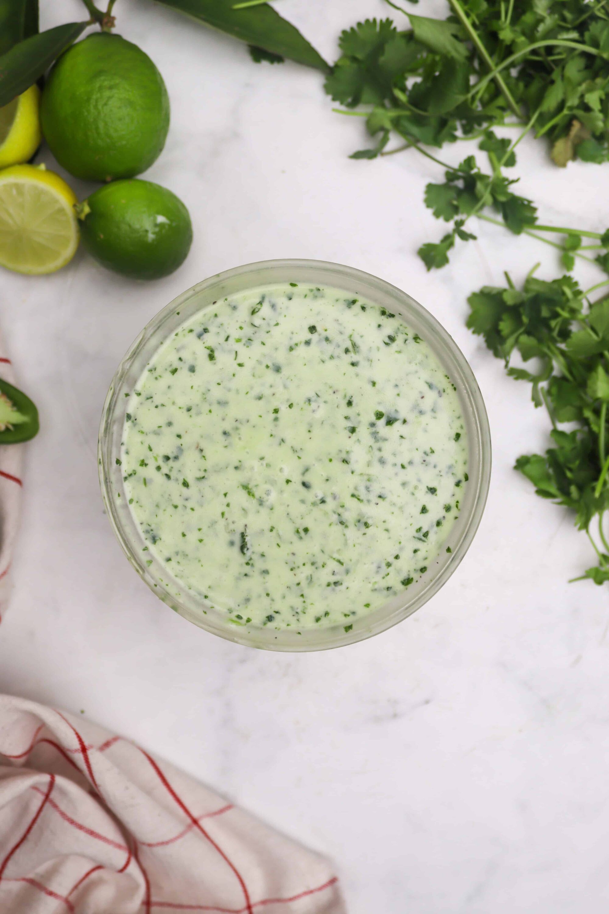 Lime cilantro dressing with creamy texture on a white background with fresh herbs.