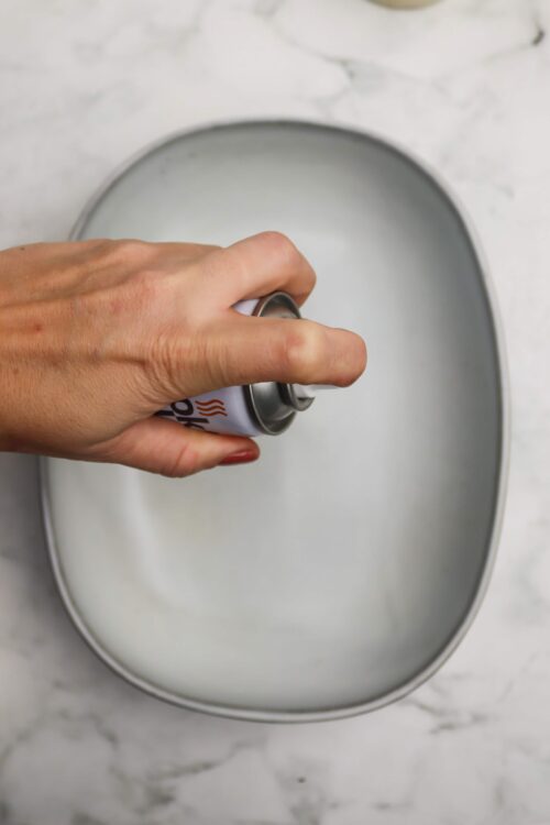 Canned whipped cream being sprayed onto a dessert on a white tray.