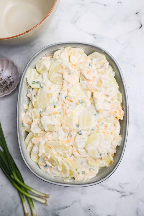 Creamy potato salad with green onions in a baking dish, ready for serving.