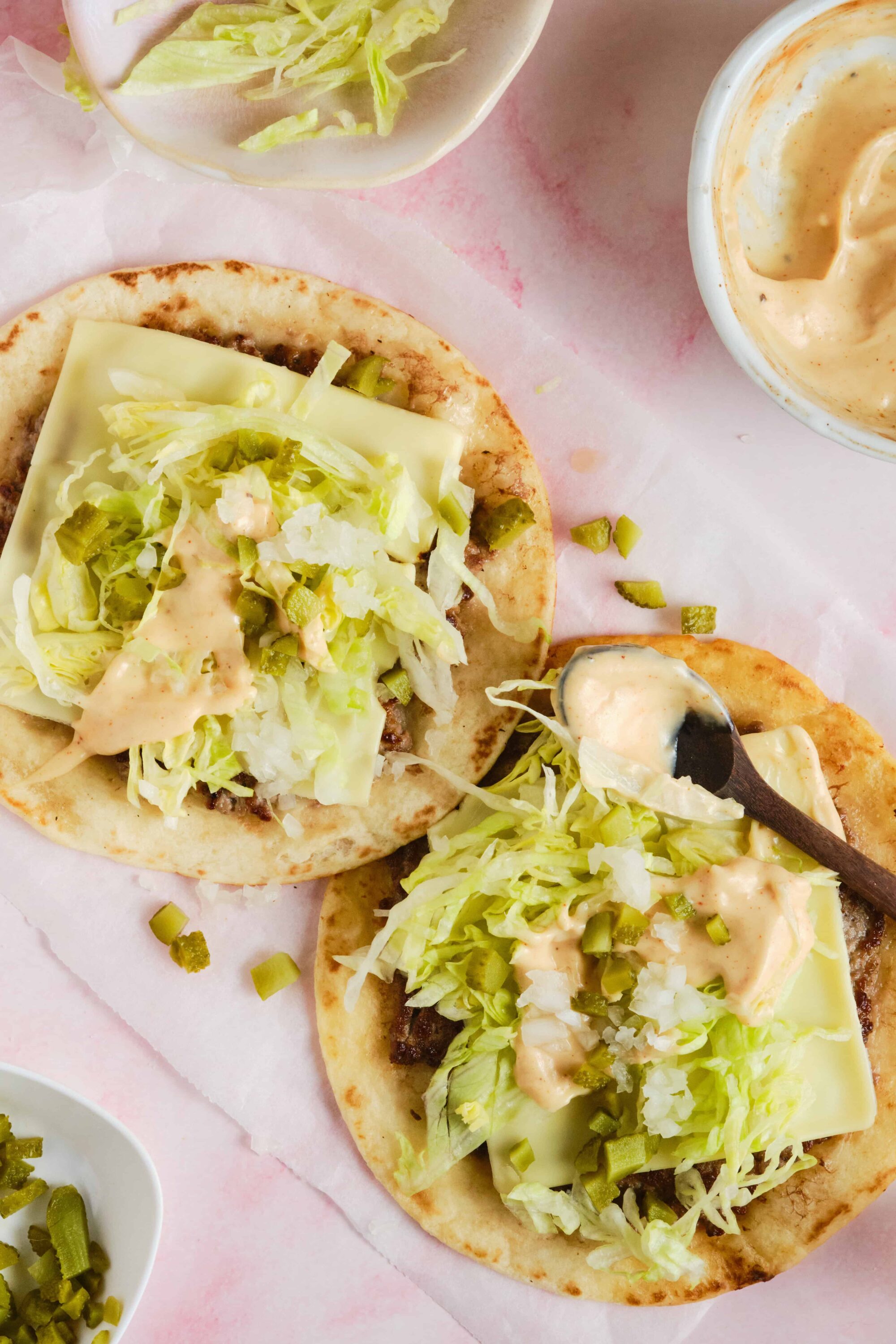 Fresh tacos with lettuce, cheese, and creamy sauce on soft tortillas, served with diced pickles and spicy mayo dipping sauce.