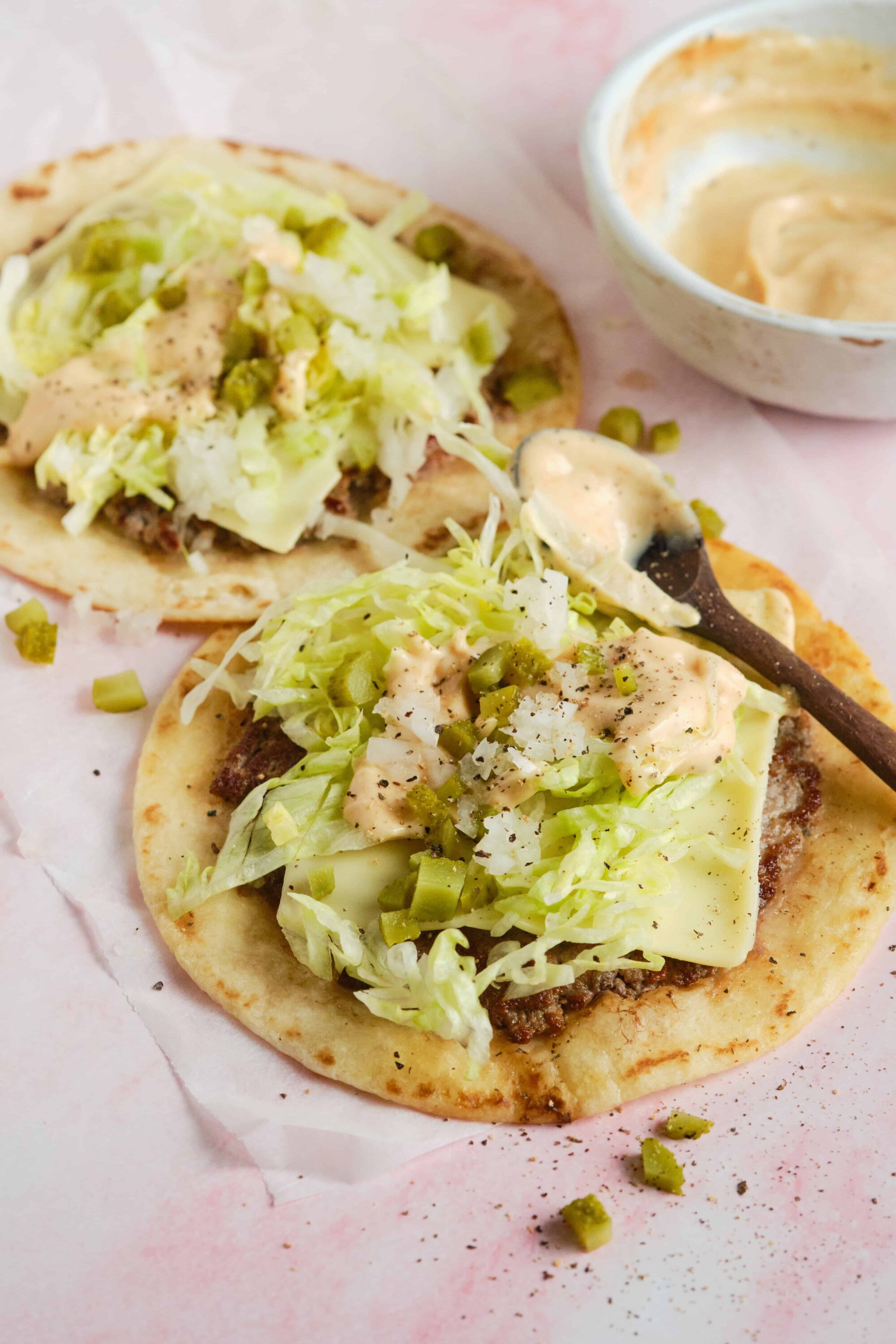 Crispy tacos with lettuce, cheese, and creamy sauce on a pink paper lining.