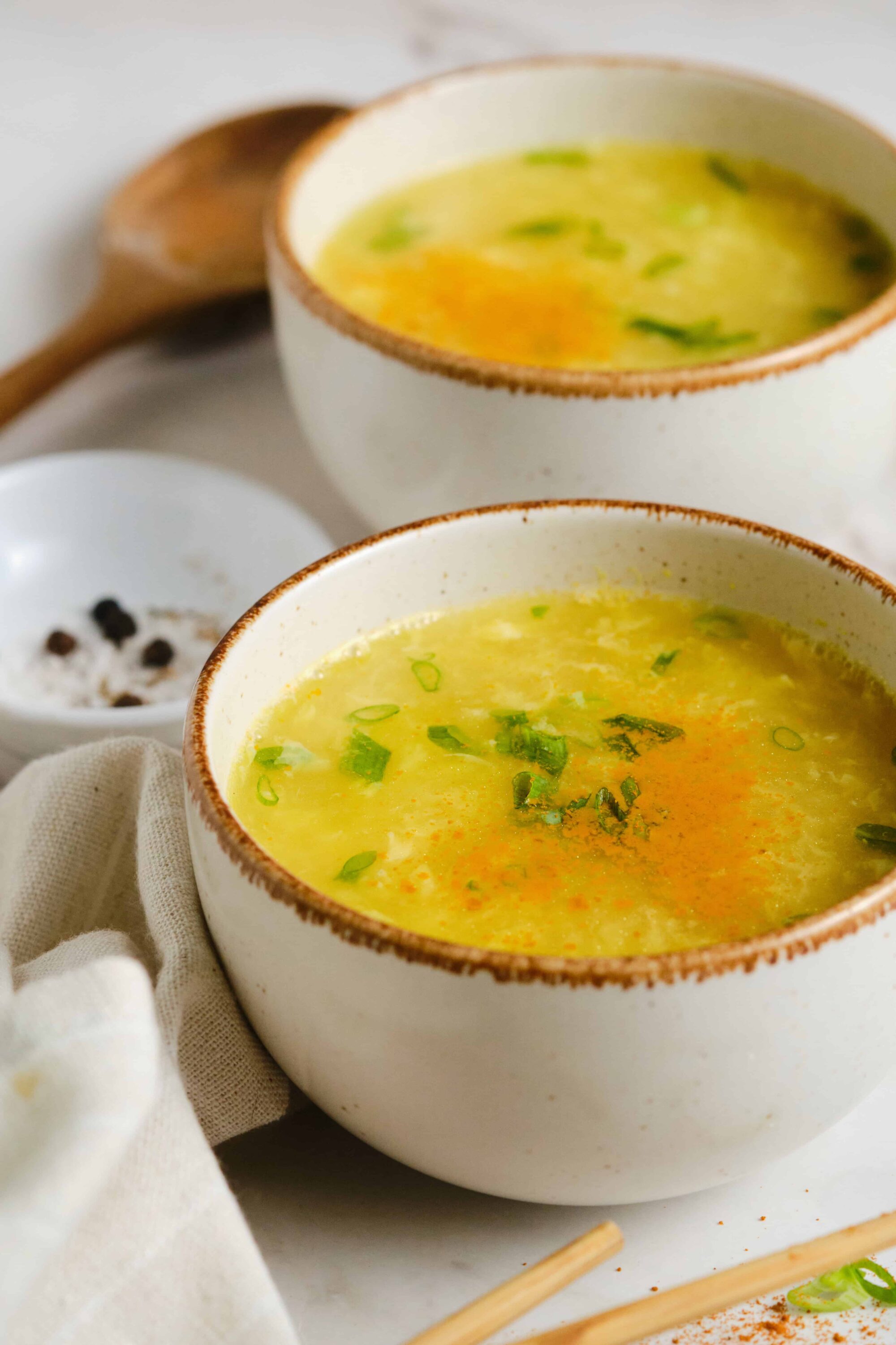 Creamy egg drop soup with chopped green onions in rustic white bowls, ready to serve.