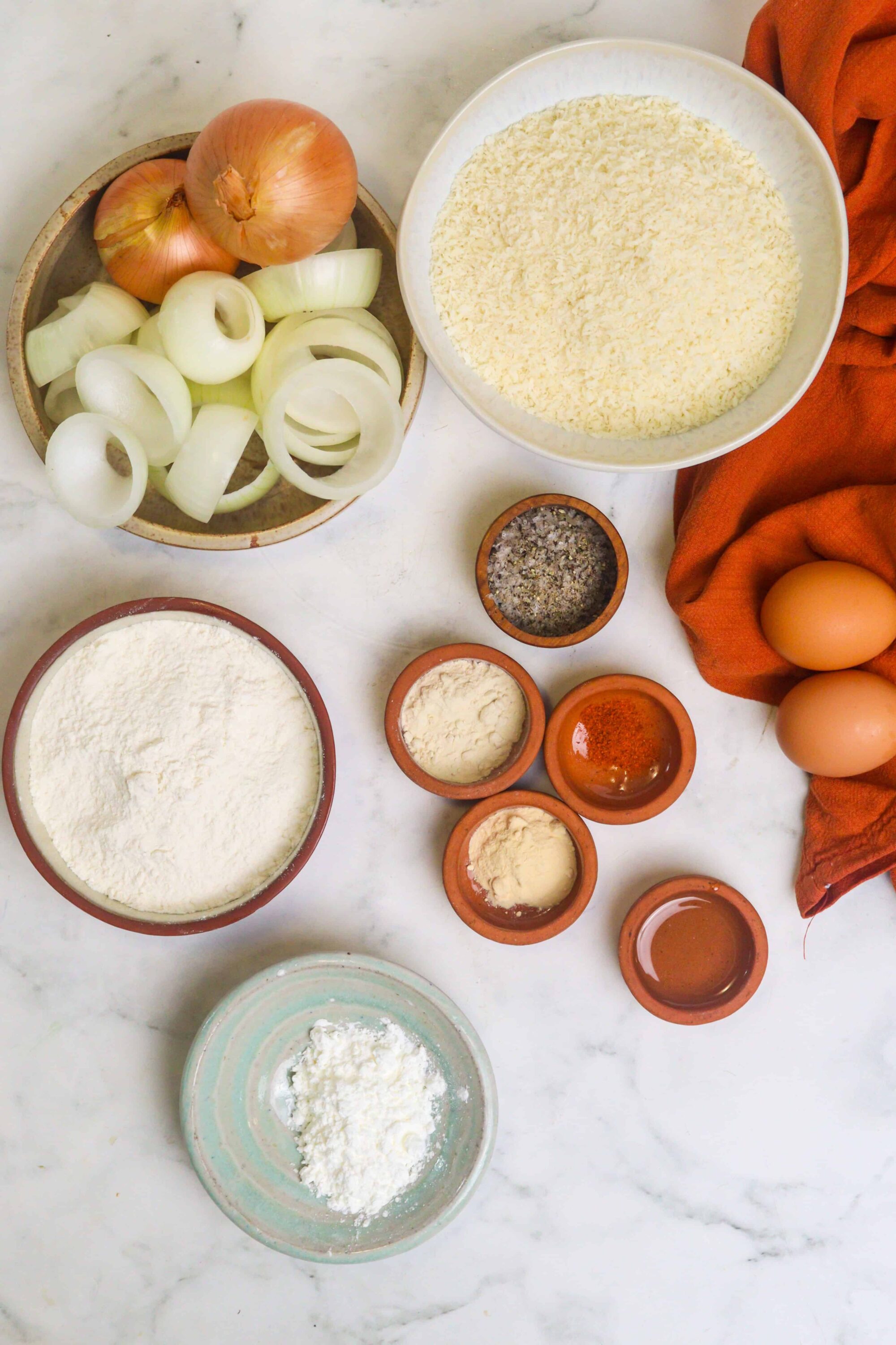 Flour, eggs, onions, and spices for baking on a white marble countertop.