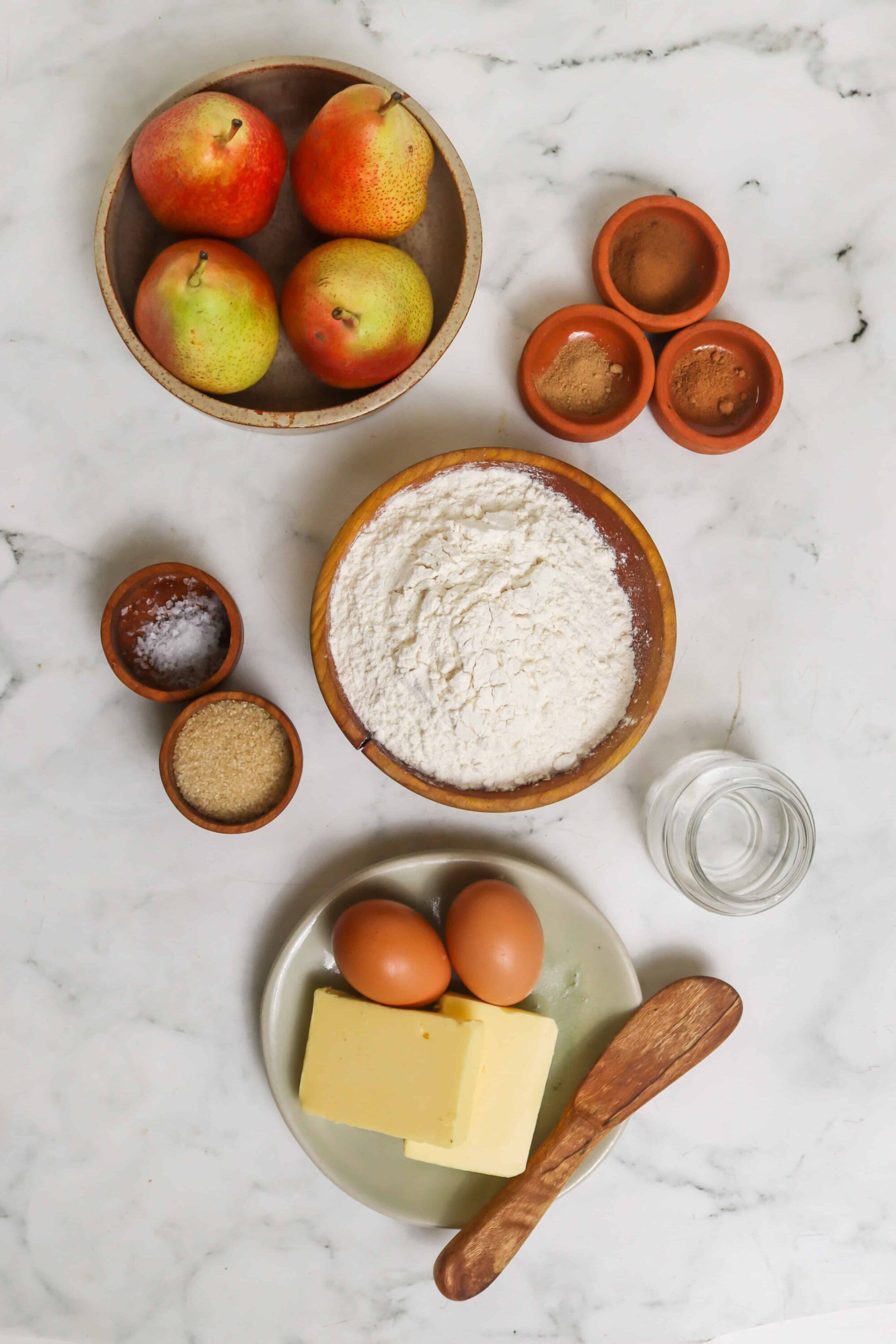 Fresh apples, flour, eggs, and baking ingredients for apple pie on marble kitchen counter.