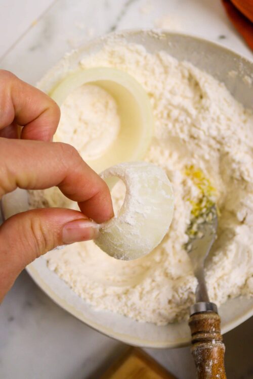 Flour and onion rings in a baking dish on a marble countertop.